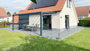 A modern house with a sloped roof, a covered patio with a table and chairs, and a brick exterior. - Holiday Home With Pet-friendly Garden (Breskens)