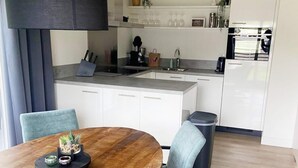 A modern kitchen with white cabinets, a wooden dining table, and a grey chair. - Holiday Home With Pet-friendly Garden (Breskens)