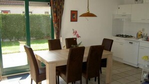 Comedor con mesa y sillas de madera, lámpara colgante y vista a un jardín a través de una puerta de vidrio.