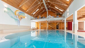 Une grande piscine intérieure dotée d’un haut plafond en bois et d’une fresque murale.