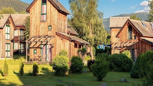 Une cabane en bois avec un toit pentu, une cheminée et un petit porche avec des chaises.