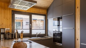 Een moderne keuken met een houten plafond, een groot raam, roestvrijstalen apparatuur en een houten kom op het aanrecht.