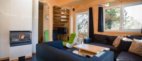 A cozy cabin interior with a fireplace, wooden walls, a sofa, and a dining table.