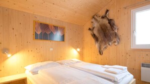 Une pièce de cabane en bois avec un lit, une peau d’animal tendue au mur et un tableau.