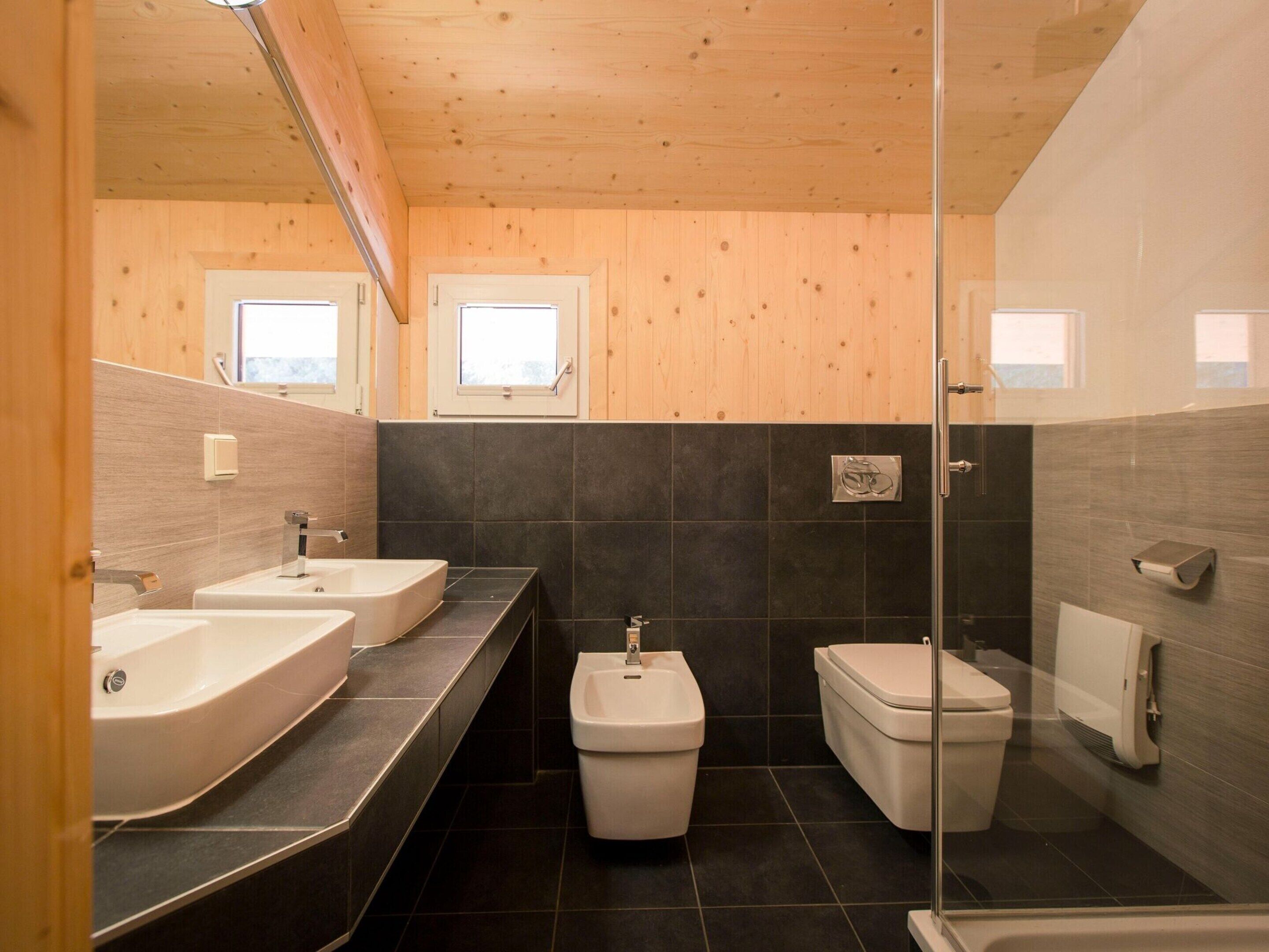 Een moderne badkamer met twee wastafels, een toilet en een douche.