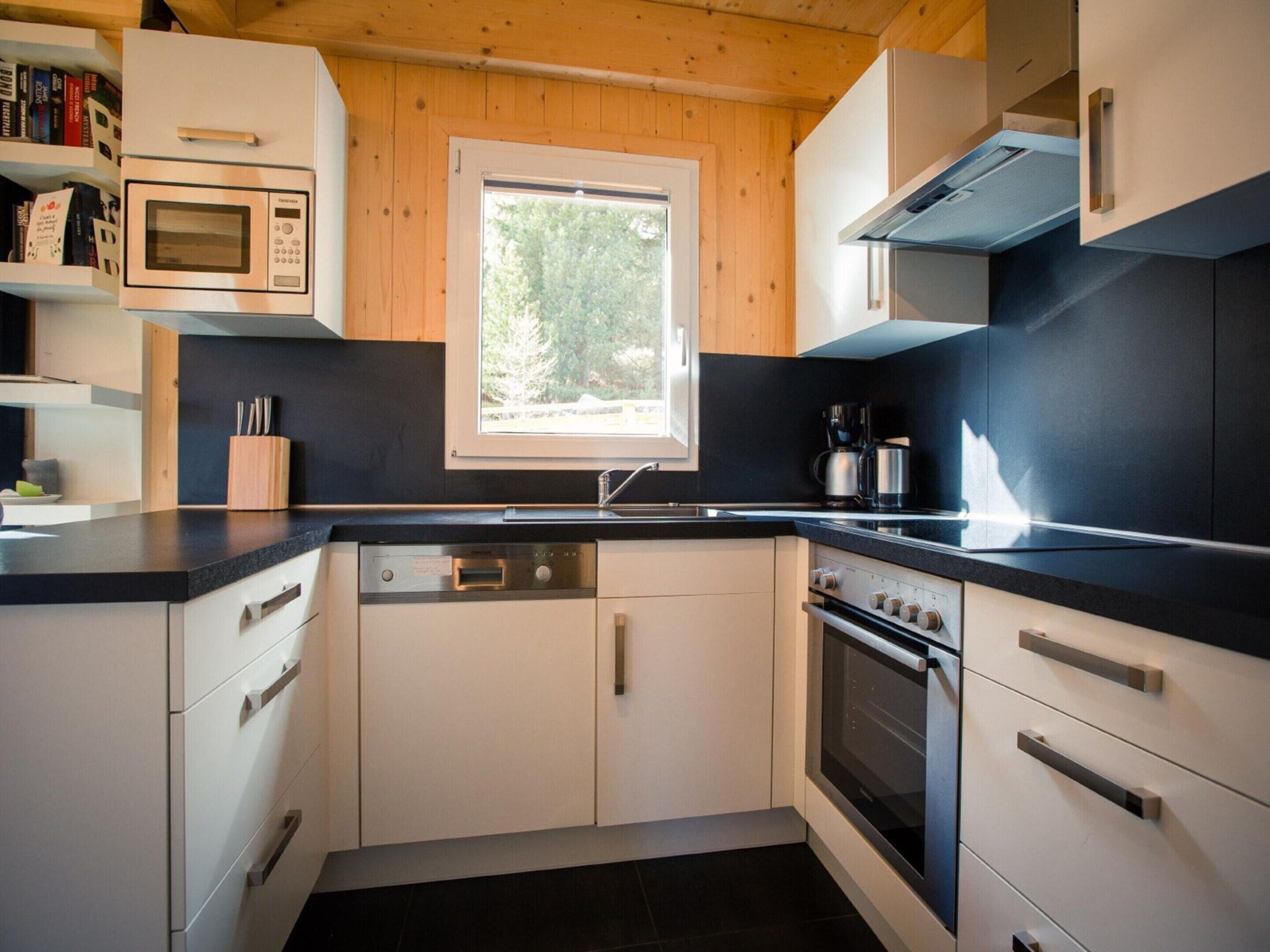 Una cocina moderna con microondas integrado, lavavajillas y horno. Hay una ventana sobre el fregadero, y la cocina tiene una encimera negra y armarios blancos.