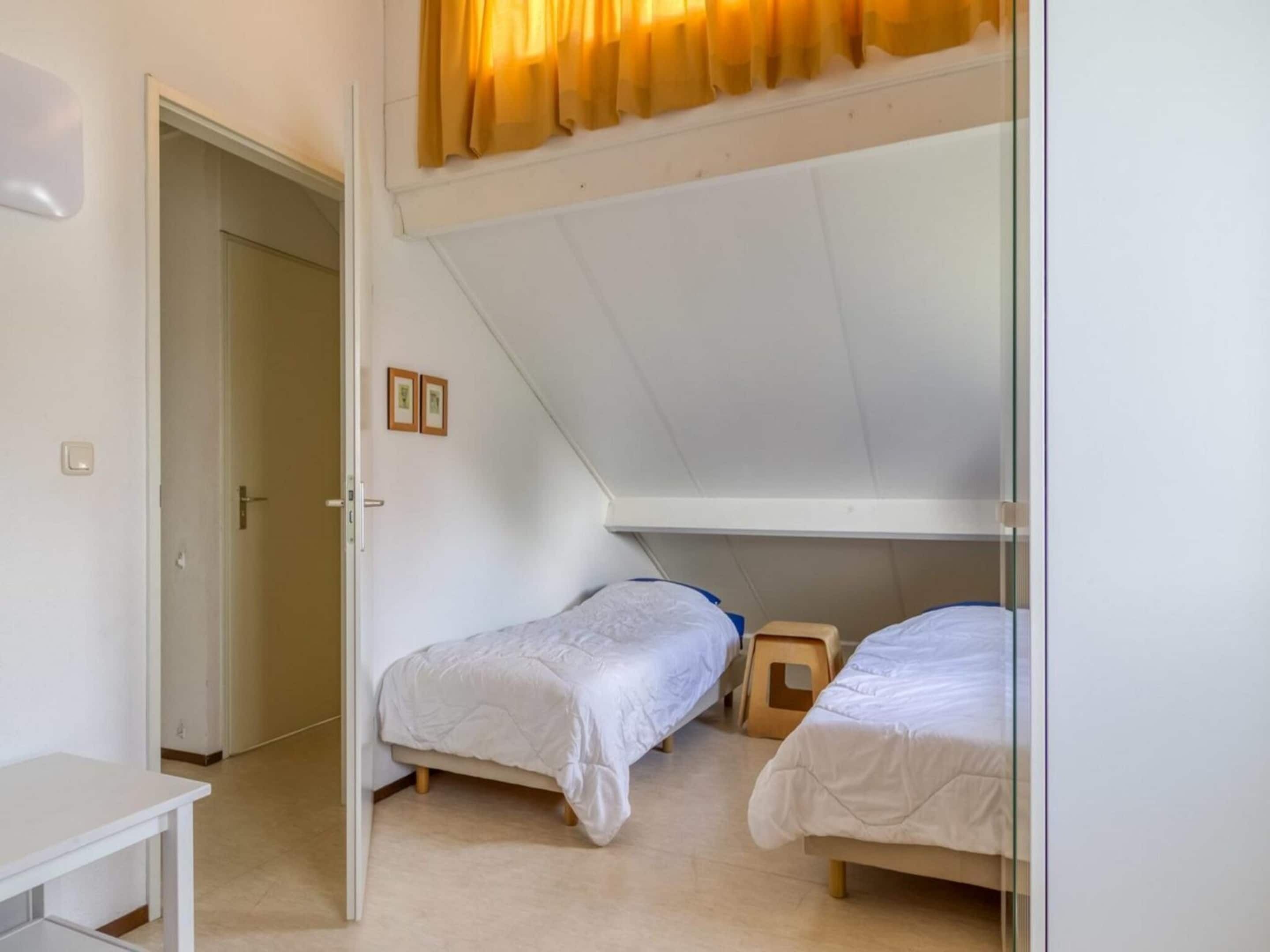 A dormitory room with two bunk beds, a small table, and a door leading to another room.