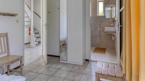 Ein Zimmer mit einer hölzernen Bank, einer weißen Tür, einem Spiegel und einem Badezimmer mit Waschbecken und Spiegel.