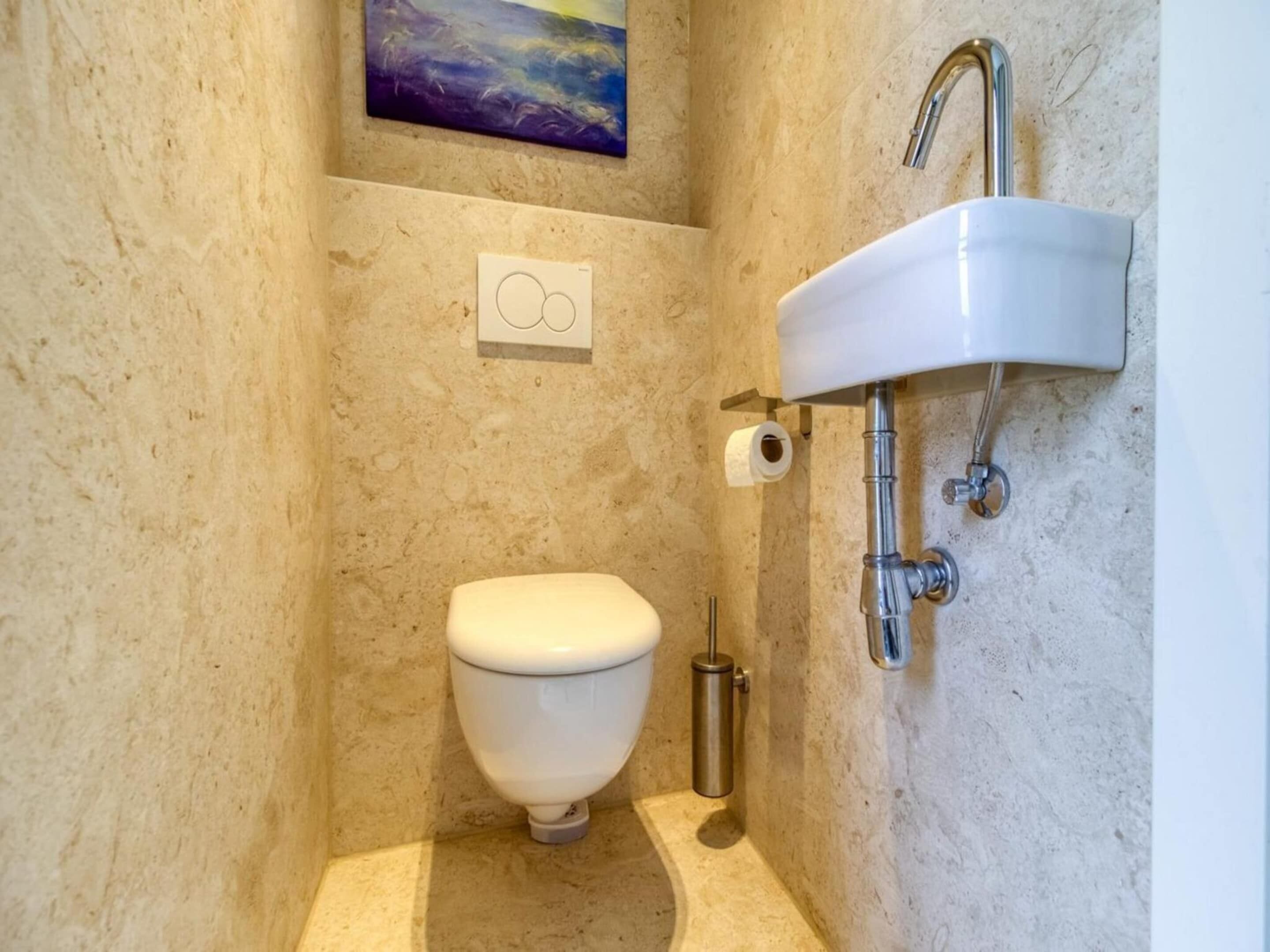 A small bathroom with a toilet, a wall-mounted sink, and a painting above the toilet.