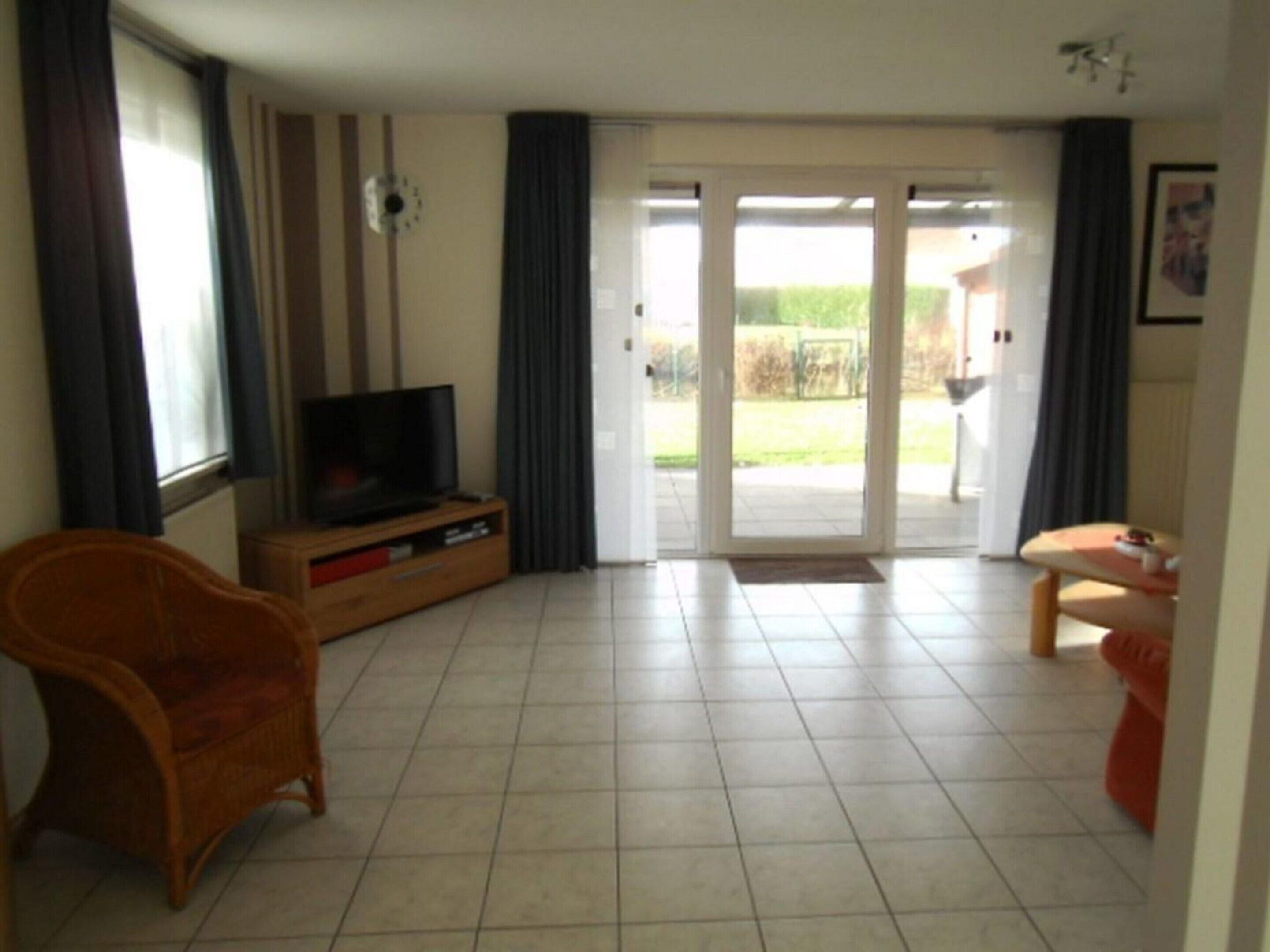 A living room with a television, a wicker chair, a small table, and a sliding glass door leading to an outdoor area.
