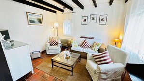 Een woonkamer met een witte bank, een witte fauteuil, een salontafel en een tv op een standaard.