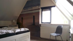 Une chambre avec un plafond en pente, un lit, une chaise, un radiateur et une fenêtre.