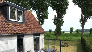 Une maison avec un toit en tuiles, une terrasse avec une table et des chaises, et une cour gazonnée avec des arbres.