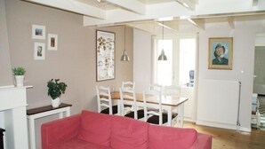 A living room with a red sofa, white chairs, a dining table, and a kitchen area in the background. - Historic Cottage w/ Garden (Breskens)