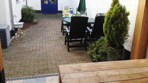 A narrow brick pathway leading to a patio area with a table and chairs, a blue door, and a small potted plant. - Historic Cottage w/ Garden (Breskens)