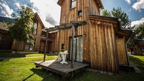 Eine Holzhütte mit geneigtem Dach, einer kleinen Terrasse mit Sitzgelegenheit und blauem Himmel.