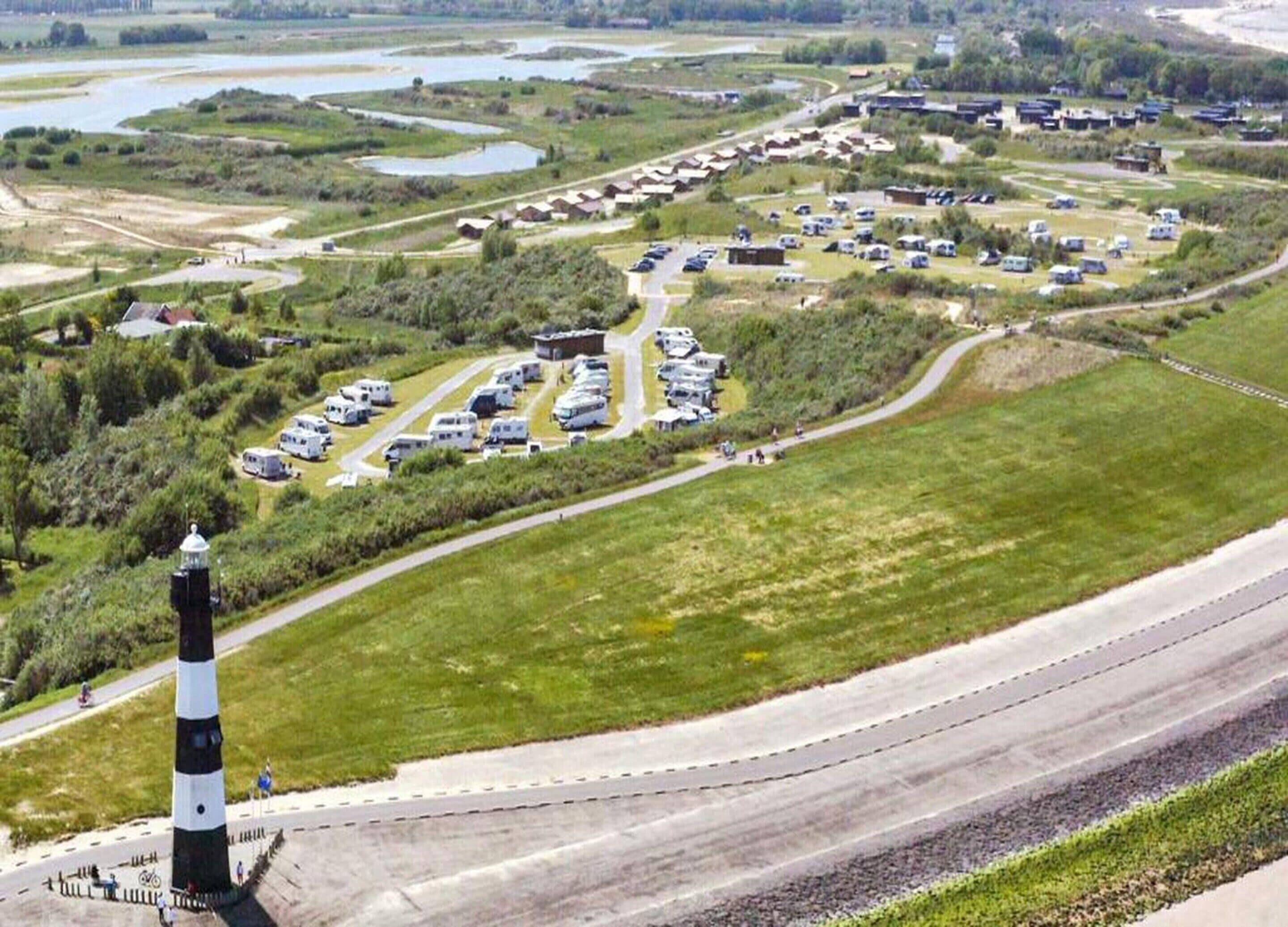 A campground with RVs parked in designated areas, surrounded by grassy fields and a body of water.