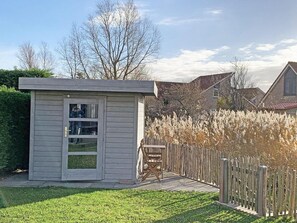 Un petit abri en bois avec une porte et une fenêtre, un banc en bois et une clôture en bois, situé dans un quartier résidentiel.