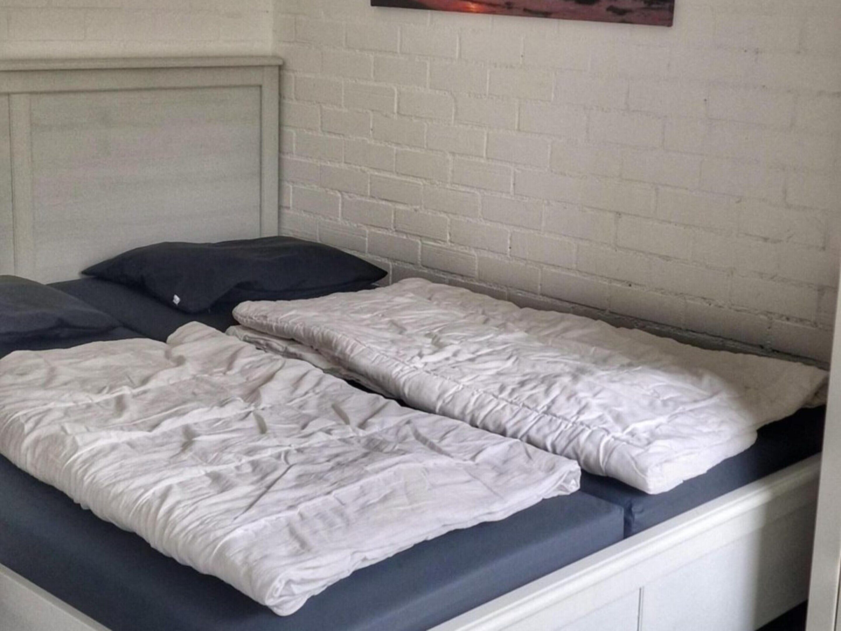 Una cama con ropa de cama blanca y un colchón azul oscuro, un cabecero blanco y una pared de ladrillo blanco.