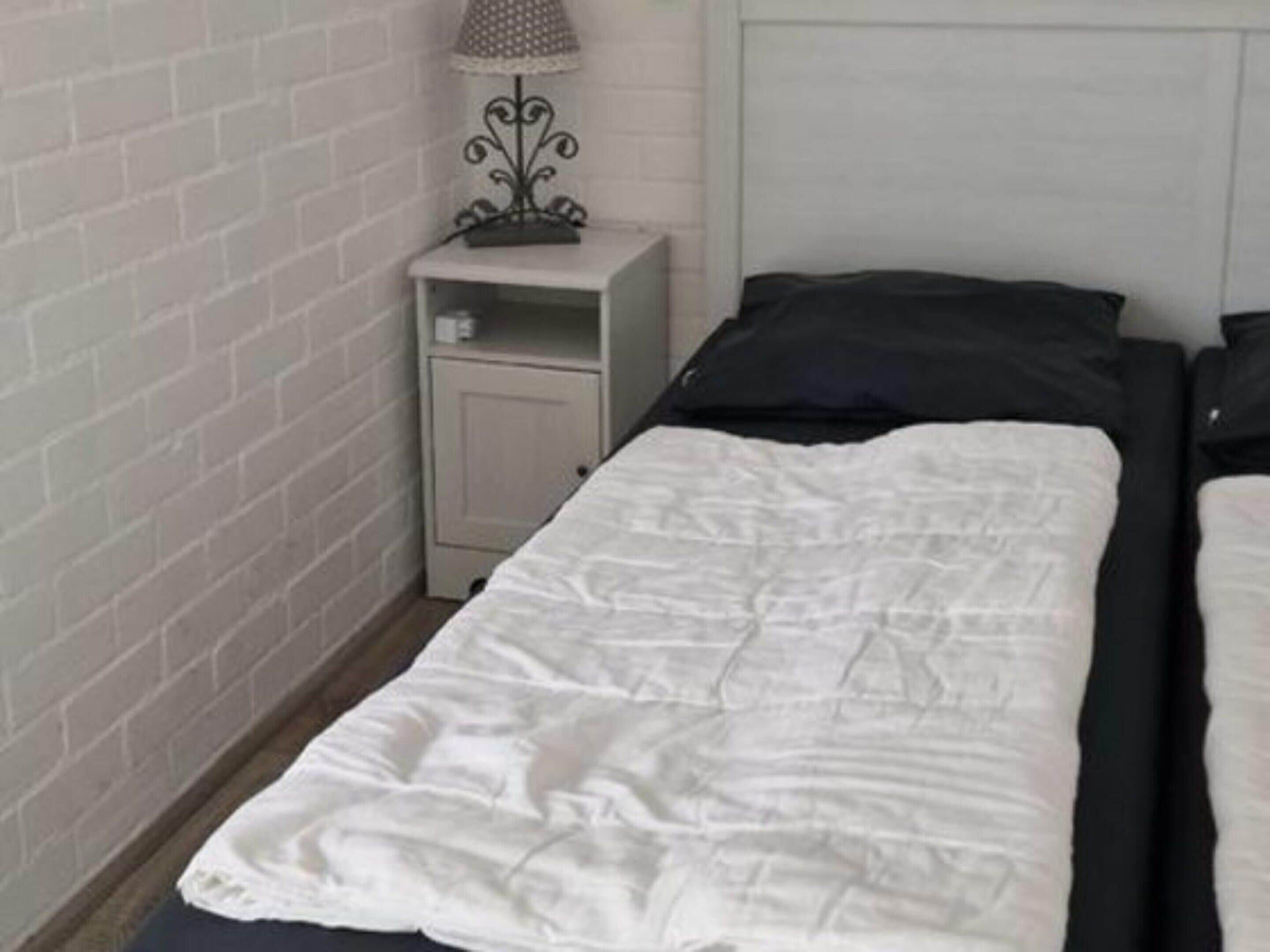 Een kamer met twee bedden, een klein nachtkastje met een lamp en een witte bakstenen muur.