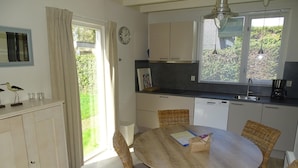 A kitchen with a dining table, wicker chairs, a clock, and a window with blinds. - Family Stay - Near Beach (Breskens)