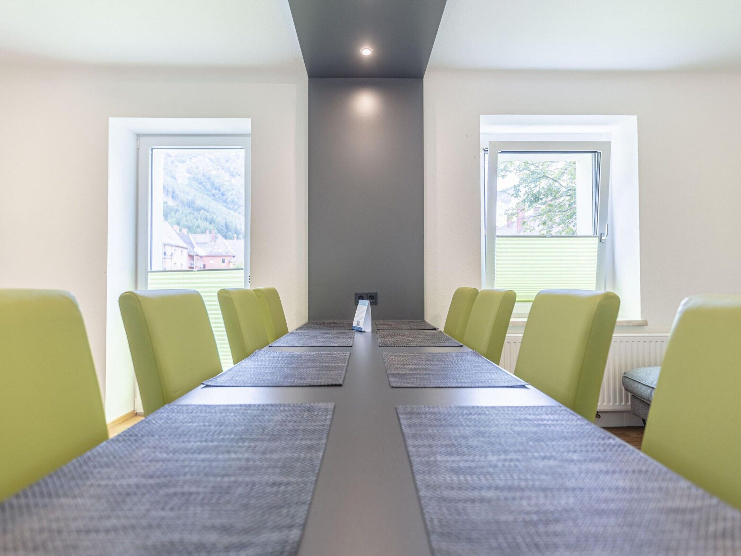 Une salle de conférence avec une longue table, six chaises et deux fenêtres équipées de stores.