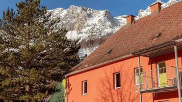 A building with a red facade and a balcony, set against a backdrop of snow-capped mountains.