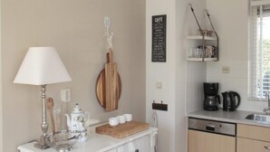 Une cuisine avec un plan de travail blanc, une machine à café, une bouilloire et une planche à découper en bois.
