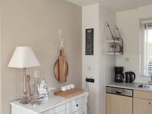 Une cuisine avec un plan de travail blanc, une machine à café, une bouilloire et une planche à découper en bois.