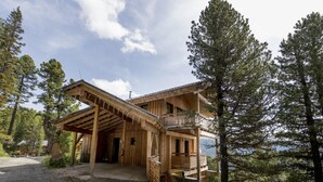 Una cabana de fusta amb un balcó, envoltada d'arbres i un camí de grava.