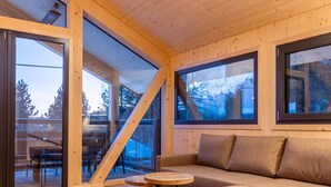 A cozy cabin interior with a wooden floor, a sofa, a small round table, and large windows offering a view of the outdoors. - Lavish Chalet With Sauna (Stadl-Predlitz)