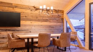 A wooden interior with a dining table and chairs, a mounted TV, and a large window with a view of a snowy landscape. - Lavish Chalet With Sauna (Stadl-Predlitz)