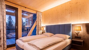 A bedroom with a large bed, wooden walls, and a view of trees through a glass door. - Lavish Chalet With Sauna (Stadl-Predlitz)