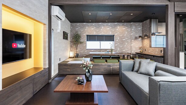 Un salon moderne avec un téléviseur à écran plat, une table basse en bois, un canapé gris et un mur orné d’un motif.