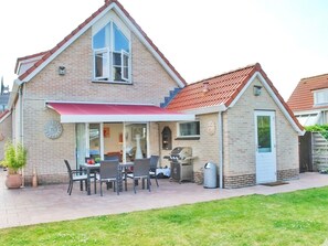 A two-story house with a red roof, a covered patio with outdoor furniture, and a brick exterior. - Spacious Stay Near the Sea (Breskens)