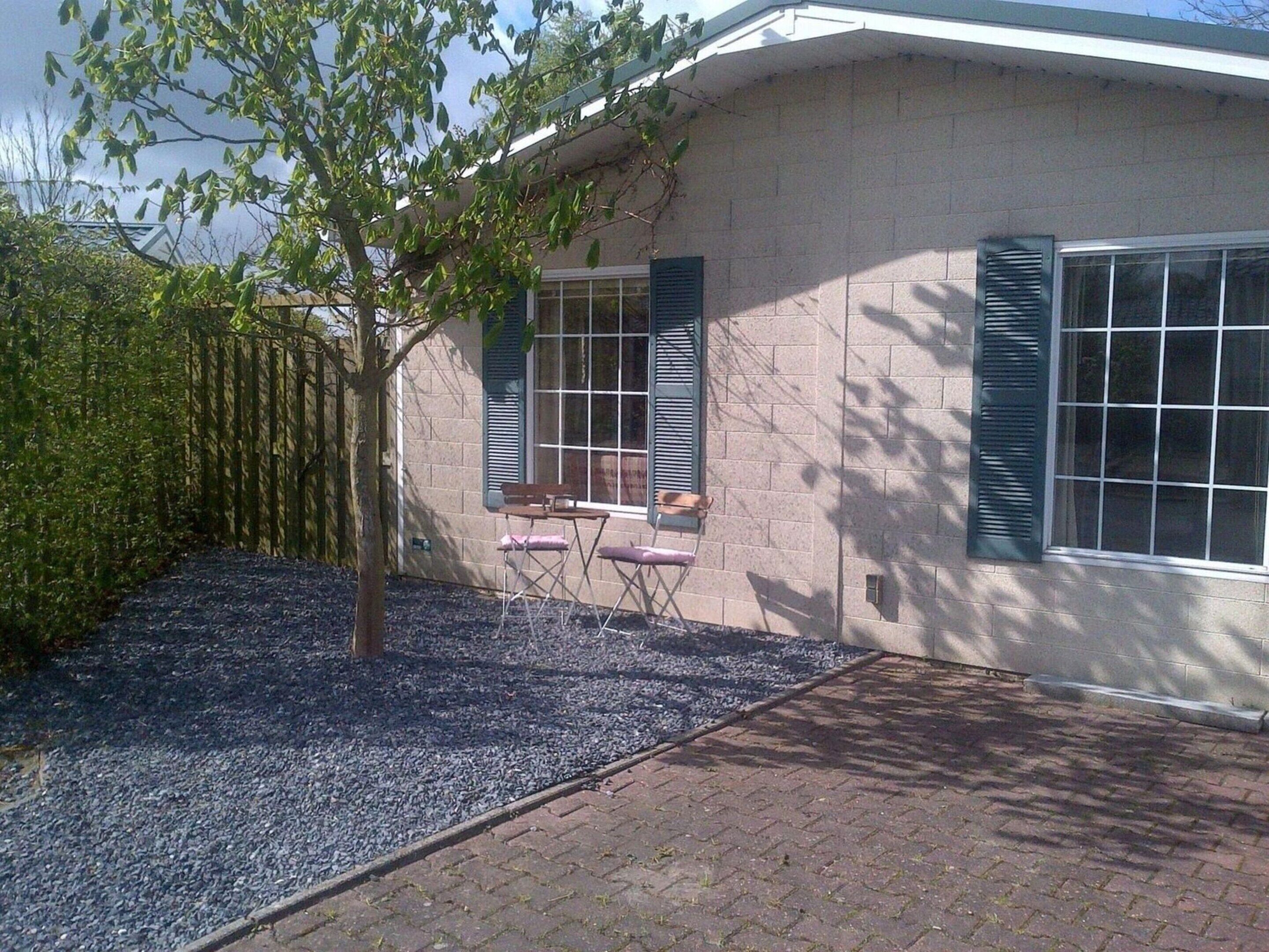 A house with a brick exterior, a tree in the front yard, and a gravel pathway leading to the entrance.