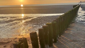 Un coucher de soleil sur une plage, avec une barrière en bois.