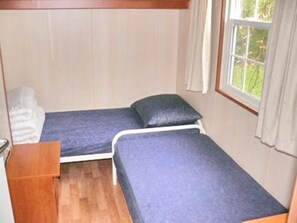 A small, compact room with two single beds, a wooden bench, and a window with a view of greenery. - Holiday Home on Waterfront in Zeeland (Groede)