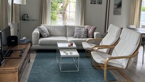 Un salon moderne comprenant un canapé, deux fauteuils, une table basse, un téléviseur et une lampe.