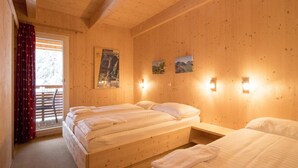 Quarto de cabana de madeira com duas camas, teto de madeira e janela com cortinas vermelhas.