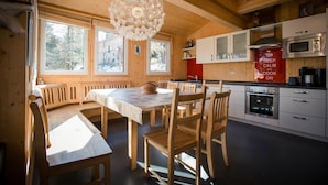 Un intérieur en bois comprenant une table à manger, des chaises, un luminaire suspendu et un coin cuisine avec des placards et des appareils électroménagers.