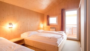 Une pièce de cabane en bois comprenant deux lits, une fenêtre et un luminaire fixé au mur.