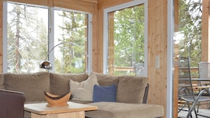 Un salon moderne avec un canapé d’angle, une table basse en bois et de grandes fenêtres donnant sur la verdure.