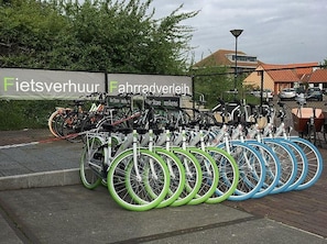 A bike rental station with multiple bicycles, a sign with text, and a fence.