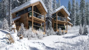 A modern wooden cabin with a balcony, surrounded by snow-covered trees.