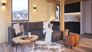 A cozy living room with a wooden ceiling, a gray sofa with decorative pillows, a round wooden coffee table, and a leather ottoman.