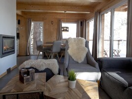 Un interior de cabaña acogedor, con chimenea, zona de comedor y amplias ventanas.