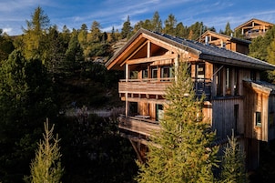 A wooden cabin with a balcony, surrounded by dense forest.