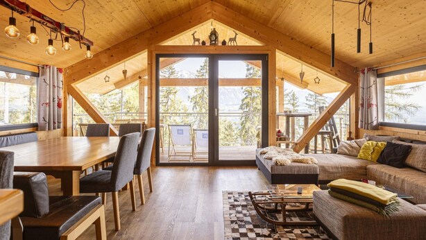 A spacious loft-style room with a high ceiling and wooden beams, featuring a dining area, seating area, and a large sliding glass door leading to a balcony with a mountain view. - Nice Chalet With Finnish Sauna (Schladming)