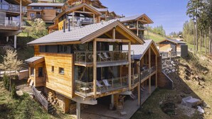 A wooden chalet with multiple balconies, a deck, and a view of a forested hillside. - Nice Chalet With Finnish Sauna (Schladming)